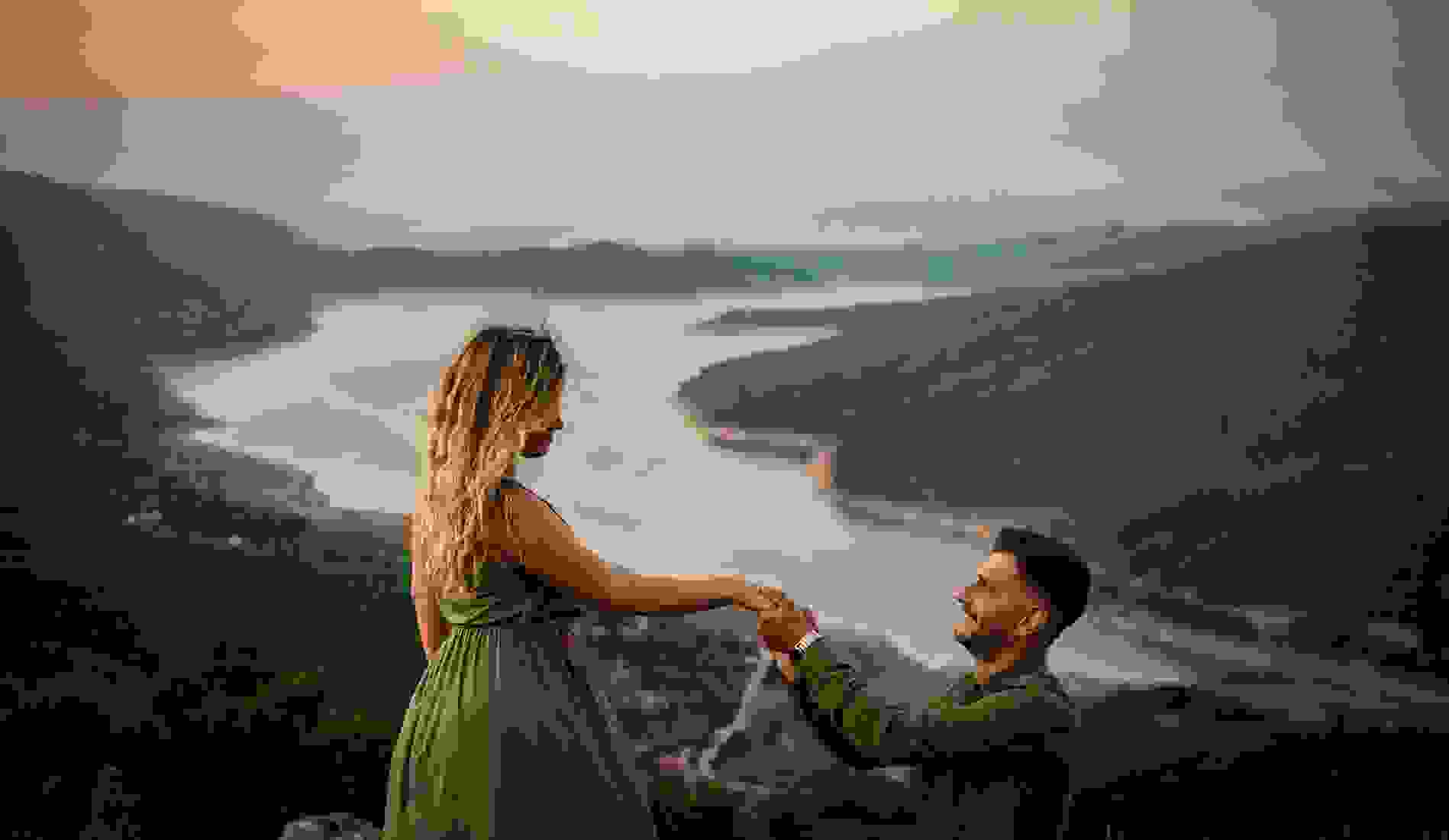 Man proposing to a woman on a mountain overlooking a winding river at sunset, creating a romantic moment with scenic natural views. 