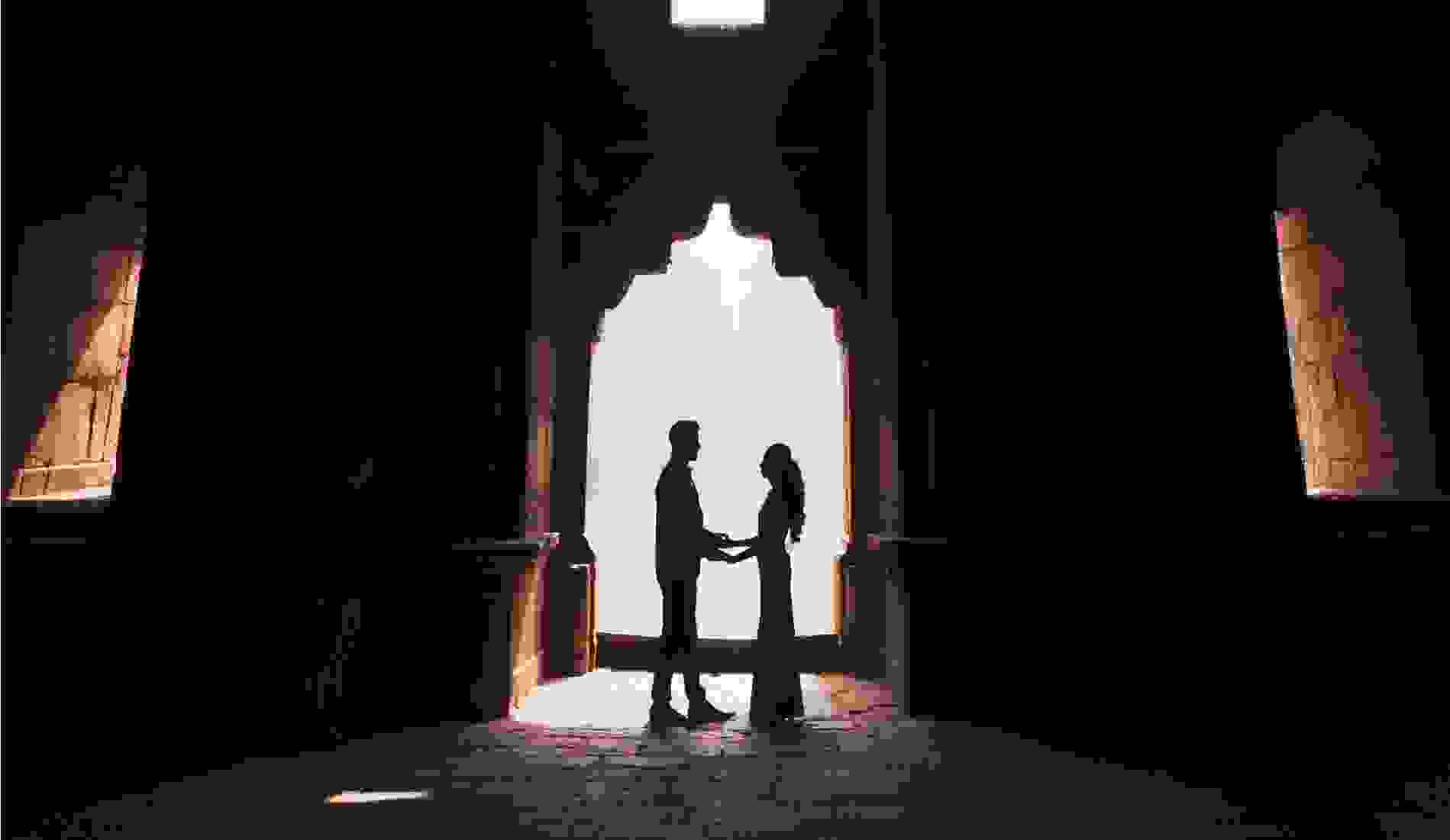 Couple standing close together on a winter evening, with the man holding an open ring box as string lights glow in the background, creating a romantic urban proposal setting. 
