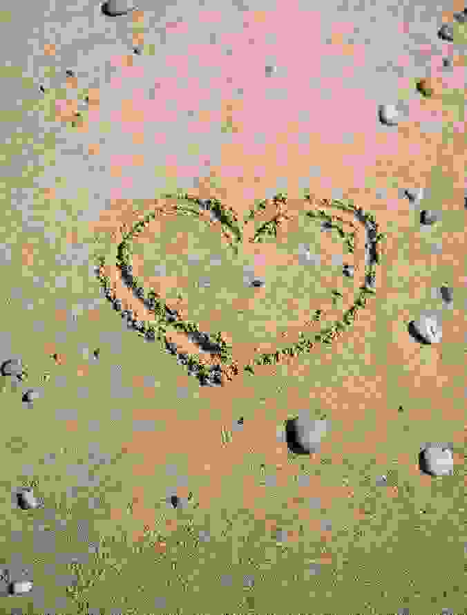 Heart shape drawn in the sand surrounded by scattered pebbles on a beach.