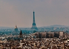 Panoramic view of Paris with the Eiffel Tower rising above the city skyline under a hazy sky.