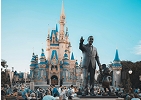 Crowd gathered in front of the Cinderella Castle at a Disney theme park, with a statue of Walt Disney and Mickey Mouse in the foreground