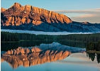 Scenic view of a mountain at sunrise reflected perfectly in a calm lake, surrounded by forest
