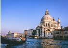 Gondola with passengers floating along a canal in Venice, with the historic Basilica di Santa Maria della Salute in the background