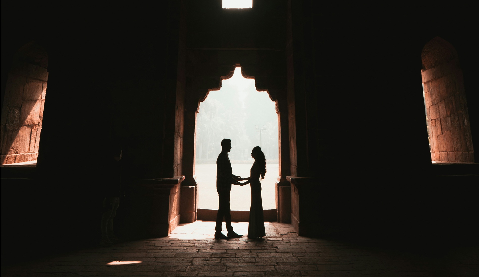 Couple standing close together on a winter evening, with the man holding an open ring box as string lights glow in the background, creating a romantic urban proposal setting. 