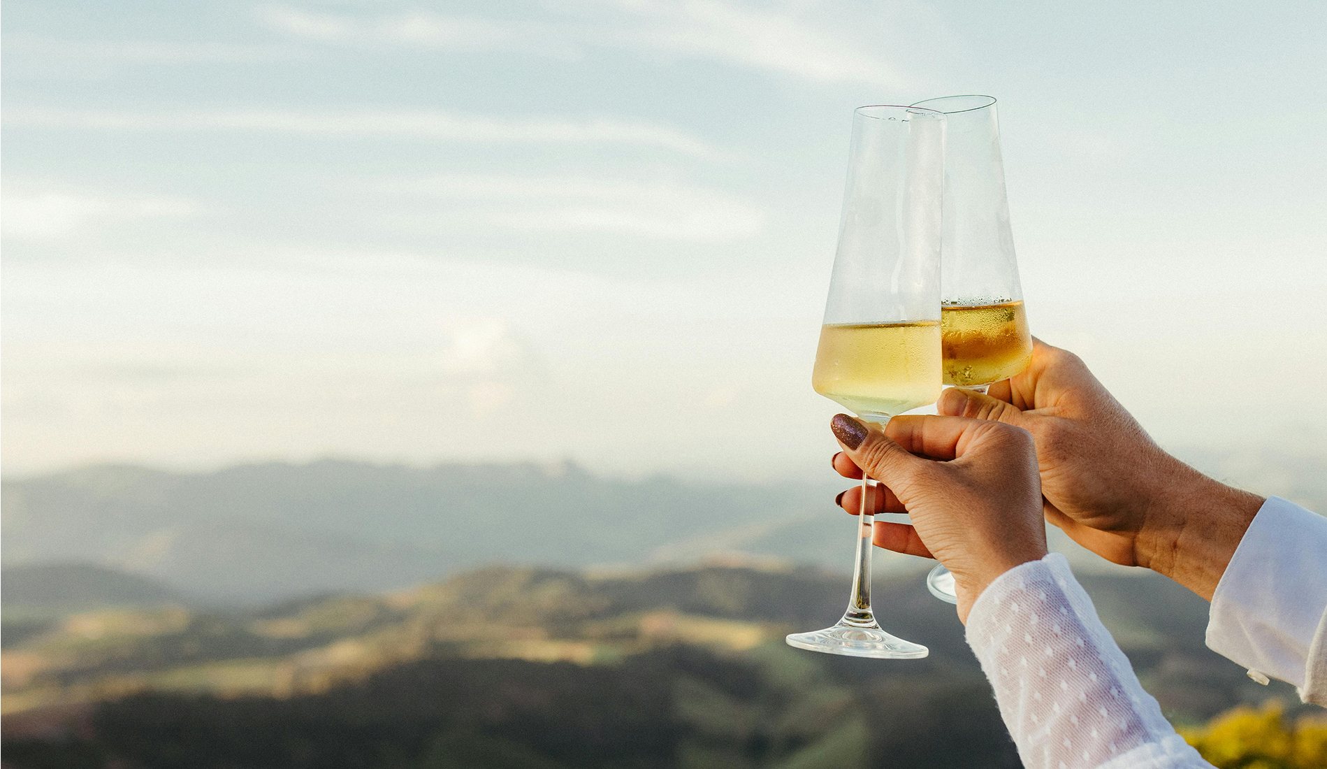 Close-up of a couple clinking champagne glasses with a scenic mountain landscape in the background, celebrating a romantic moment. .