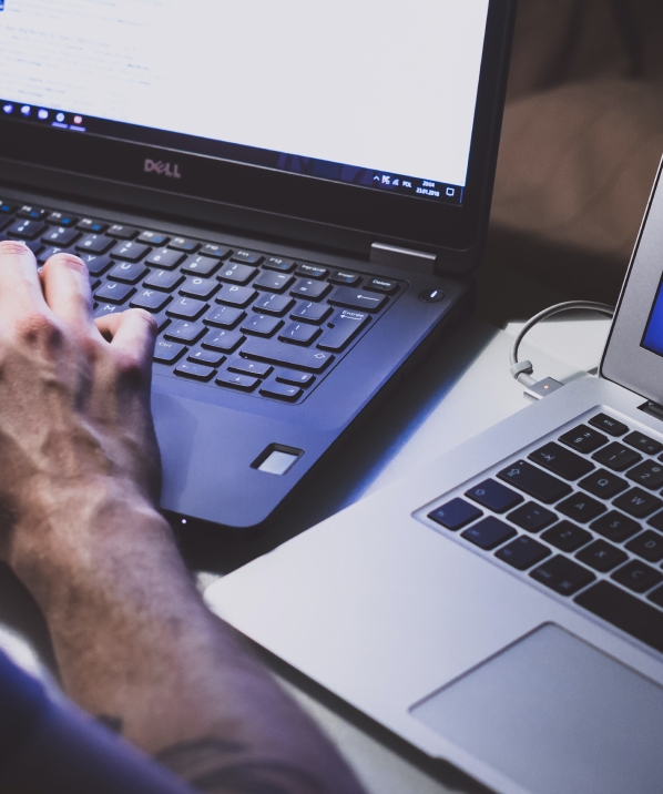 Close-up of a person working on a laptop next to another open laptop, suggesting online activity or browsing.